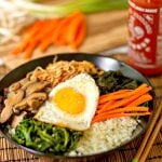 This amazing Korean Cauliflower Bibimbap recipe is delicious, low-carb, keto friendly, and easy to make. The perfect quick vegetarian weeknight dinner idea. Black bowl, bobimbap, sriracha