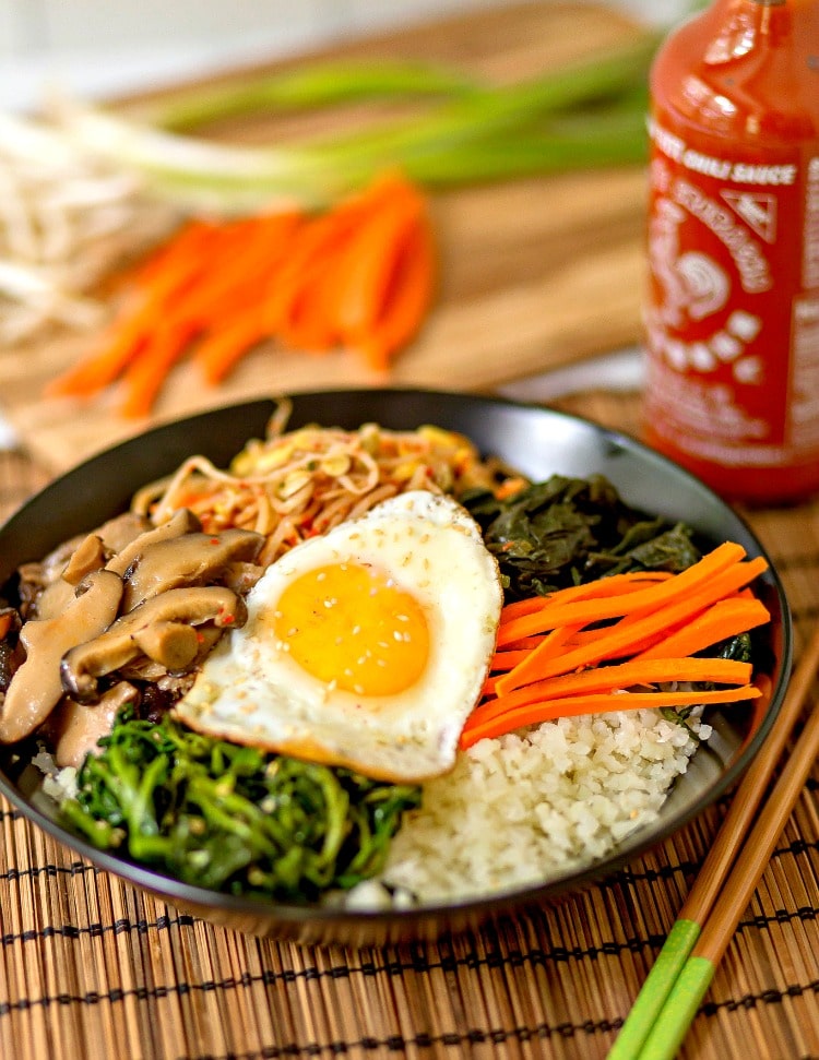 This amazing Korean Cauliflower Bibimbap recipe is delicious, low-carb, keto friendly, and easy to make. The perfect quick vegetarian weeknight dinner idea. Black bowl, bobimbap, sriracha