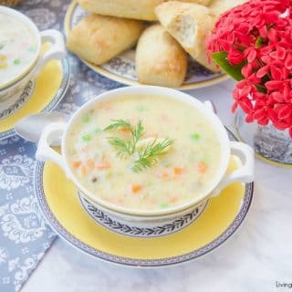This creamy Potato Dumpling Soup recipe is the perfect hearty vegetarian soup for winter. 2 bowls of soup with red flowers and fresh baked rolls