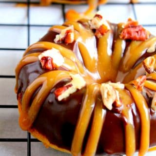These decadent Baked Turtle Donuts are are glazed with chocolate, sprinkled with toasted pecans and drizzled with sweet caramel. An irresistible dessert that tastes better than the Turtles candy bar