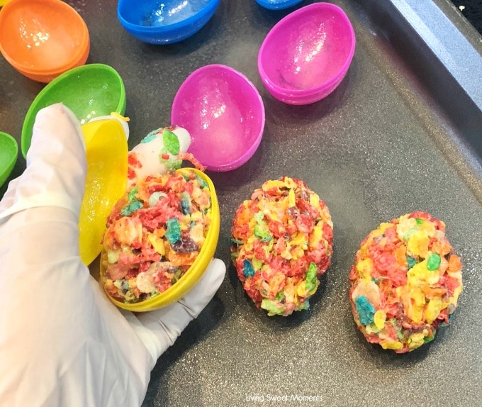 Celebrate Easter with these delicious no-bake Fruity Pebbles Eggs topped with a tangy lemon glaze. The perfect kid-friendly treat! Shaping the cereal treat using plastic eggs and latex gloves