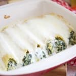 Enjoy a delicious vegetarian comfort dinner under an hour with this cheesy Spinach Artichoke Manicotti baked in a rich Bechamel sauce showing in a red square pyrex