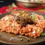 Enjoy a creamy beet risotto recipe made with roasted beets, arborio rice & goat cheese served with crispy fire-grilled chicken. Served on a wooden plate and garnished with greens